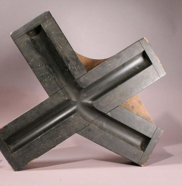 Een donker houten model met een kruisvormige holte, schuin rechtop gezet.