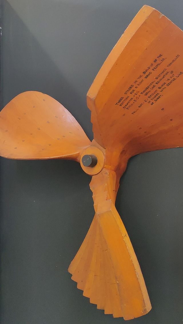 Een oranje houten gietmodel voor een scheepsschroef, met één blad nog in ruwe opbouw.